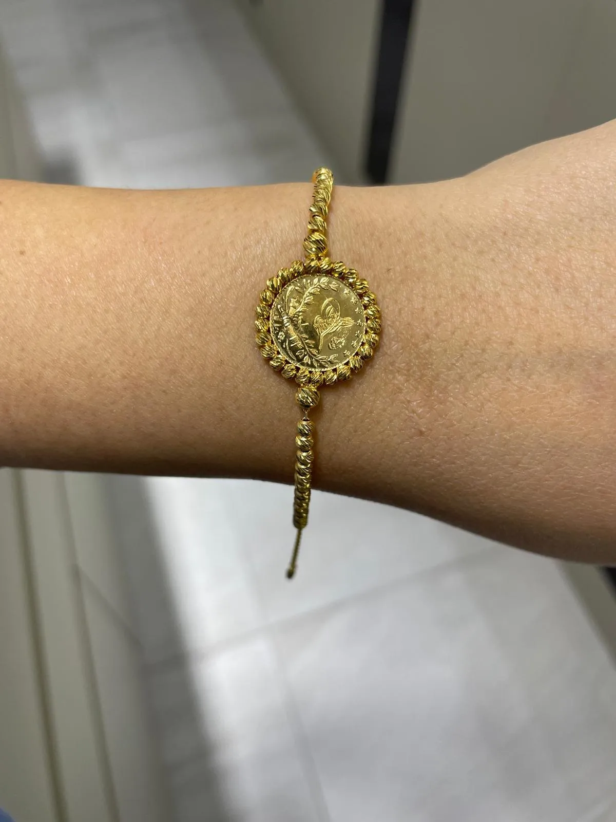 Geflochtenes goldenes Armband mit Münze am Handgelenk