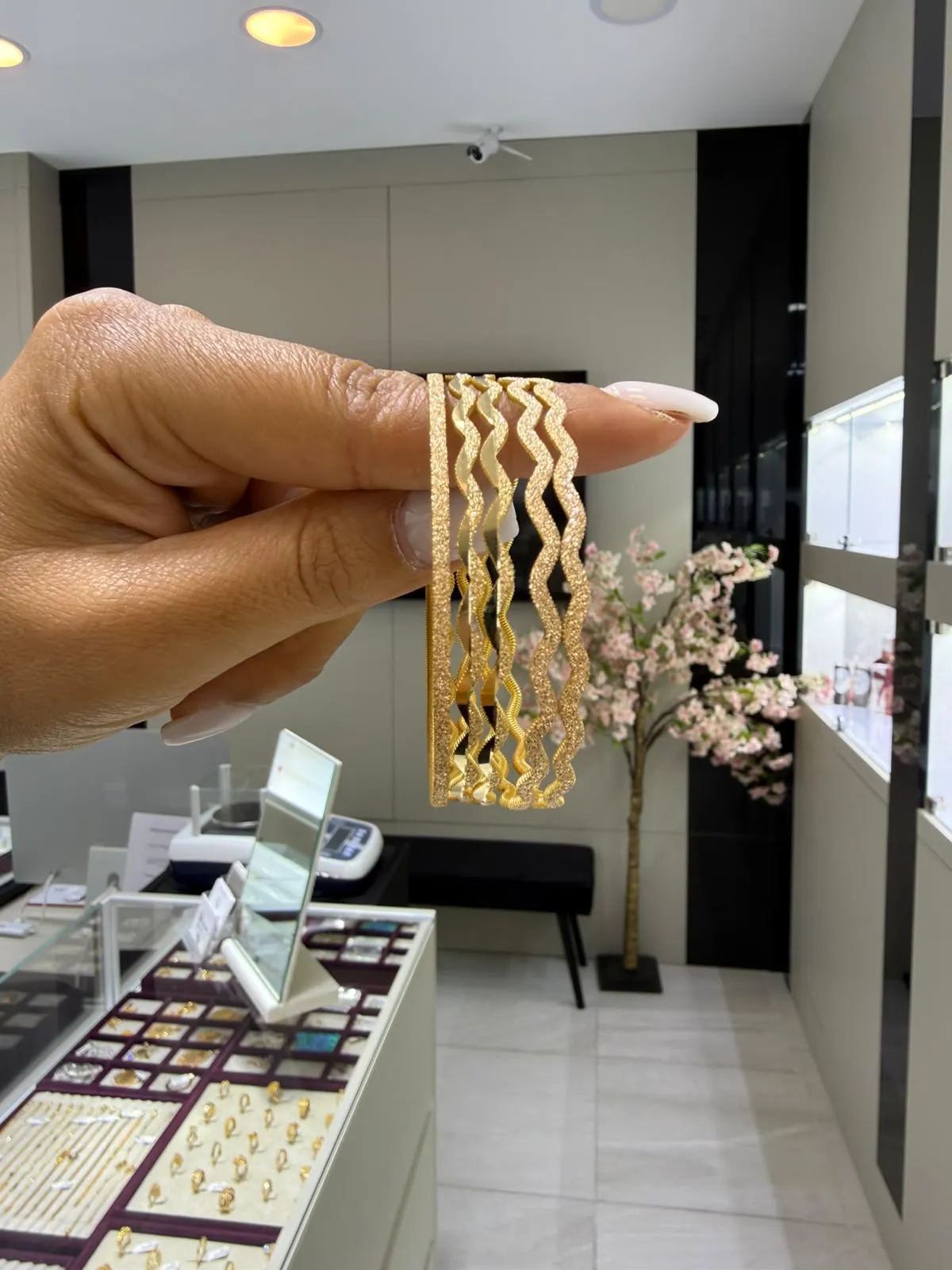 Hand hält mehrere goldene Armreifen im Geschäft von Diamond Jewels by Oya