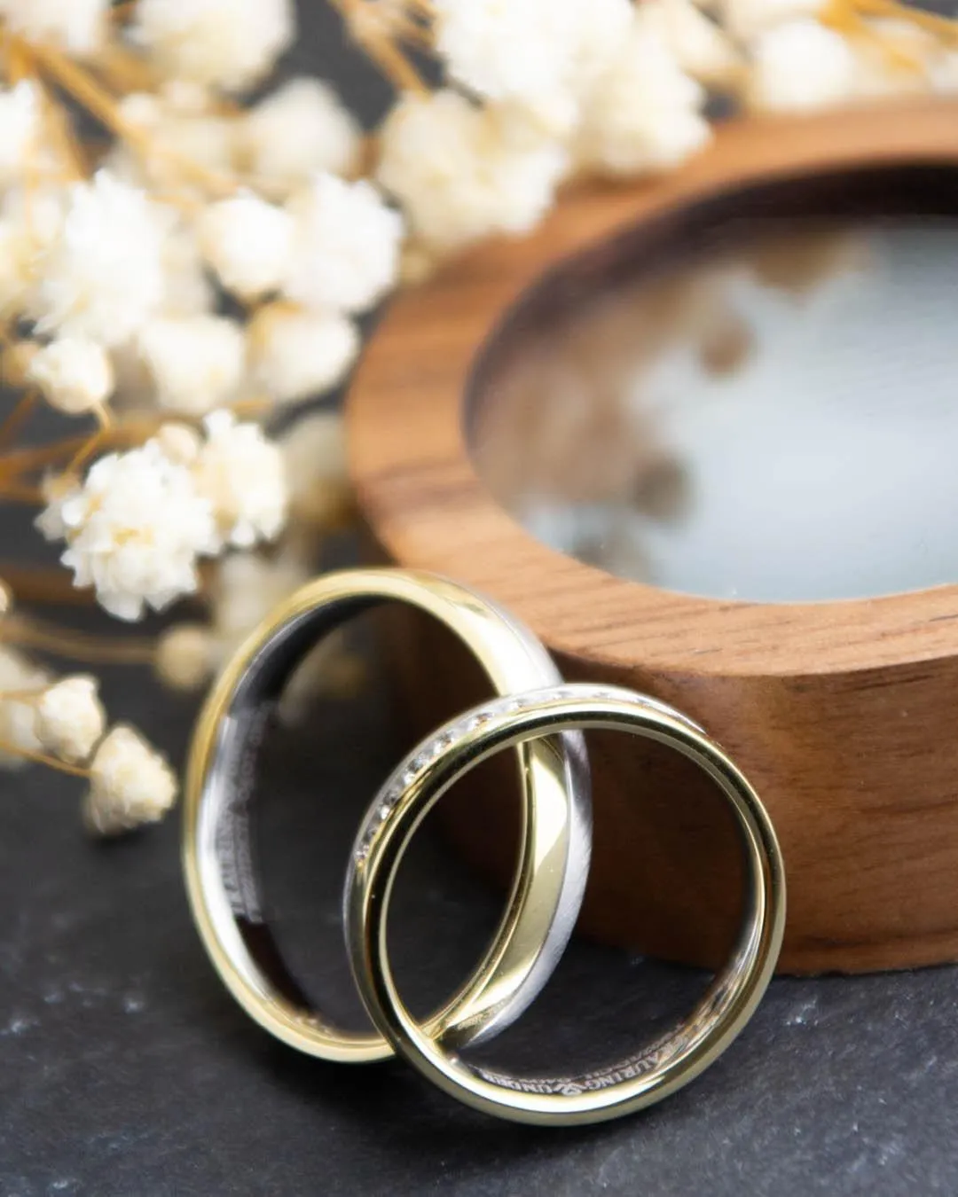 Eheringpaar in Gelb- und Weißgold mit Steinbesatz vor einer Holzschale