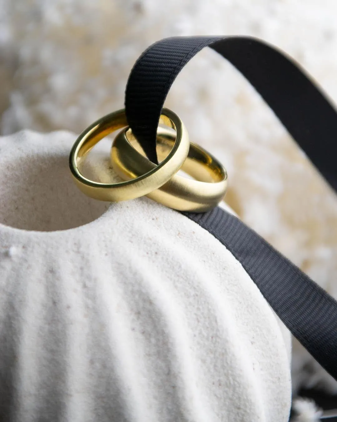 Eheringe in Gelbgold an einem schwarzen Band auf einer Keramikvase
