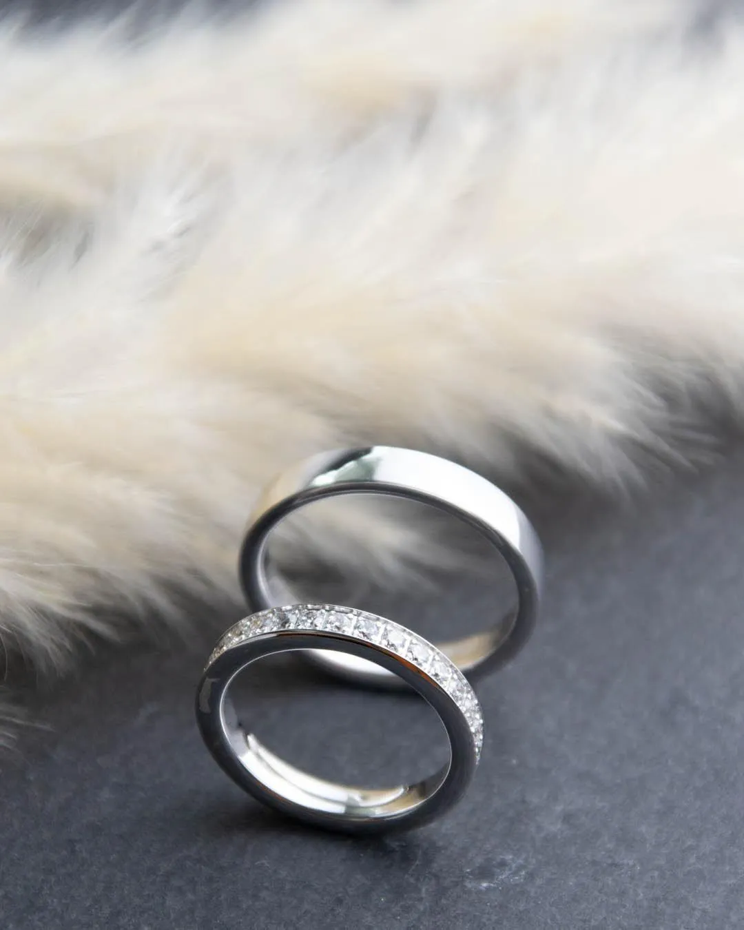Zwei Eheringe in Weißgold, einer mit Diamantbesatz, auf Schiefer vor Pampasgras