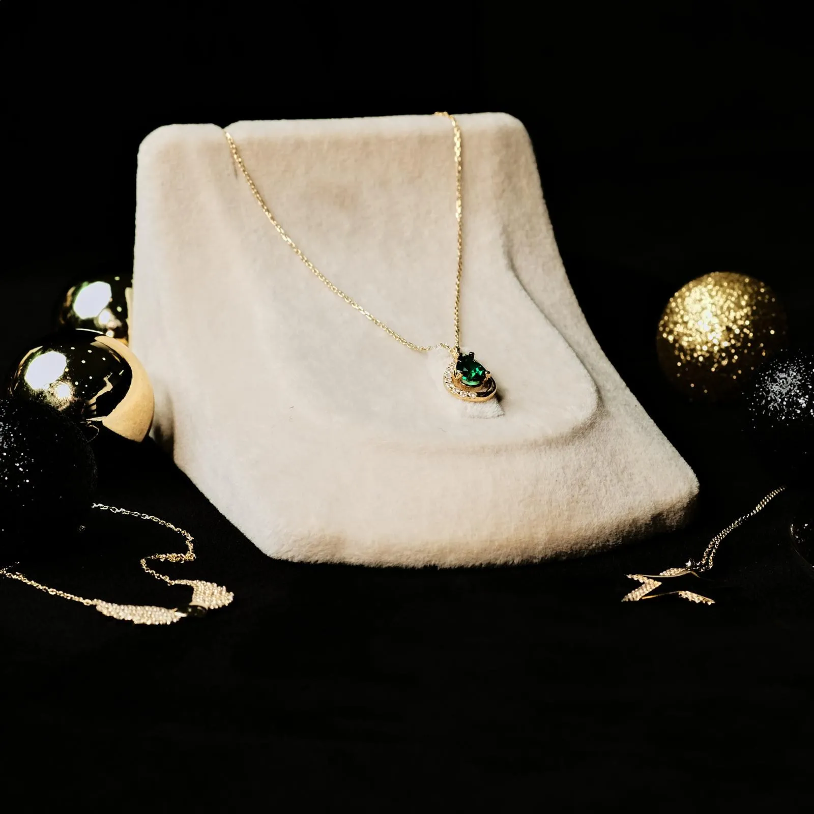 Goldkette mit grünem Tropfenstein auf hellem Samt zwischen Christbaumkugeln