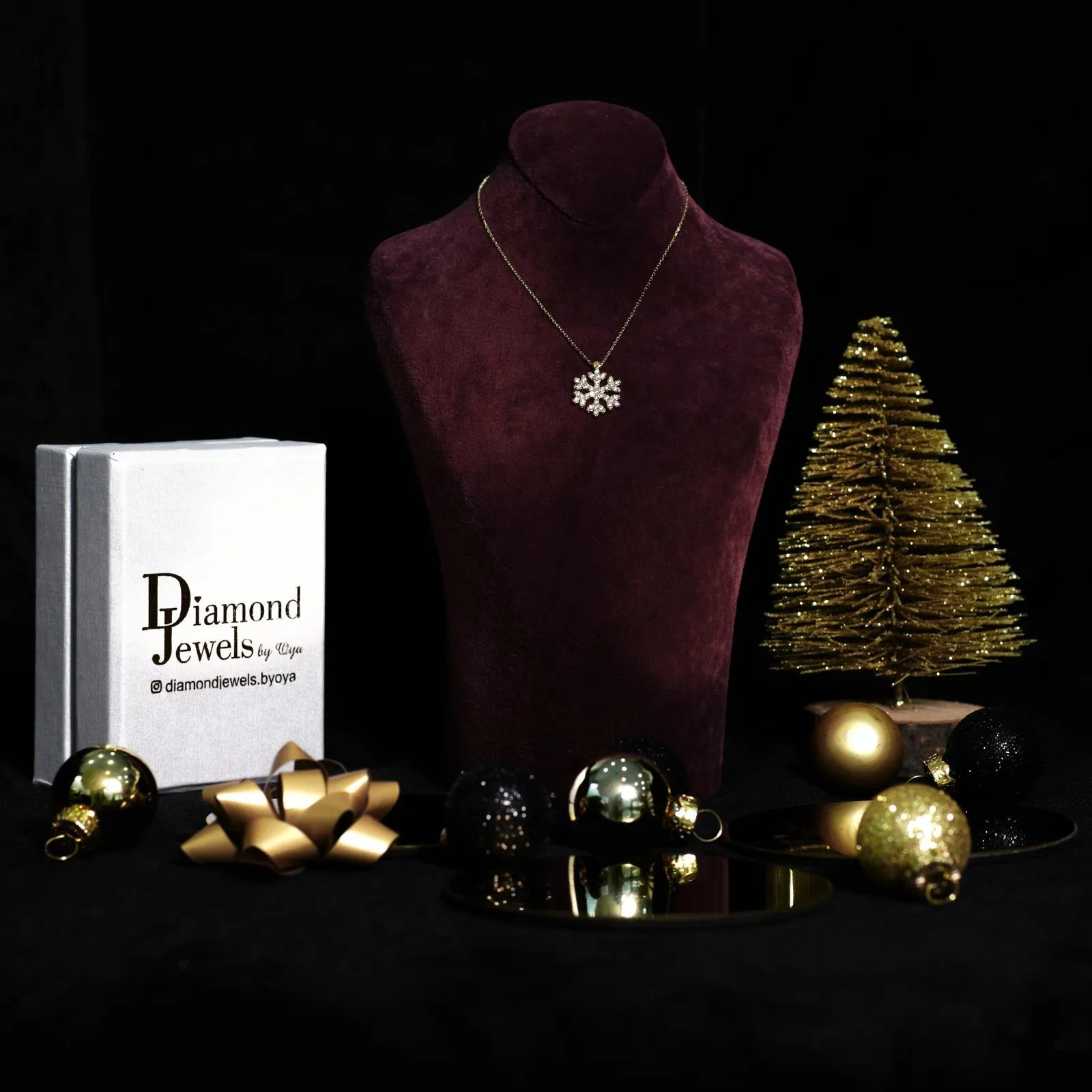 Kette mit Schneeflockenanhänger auf einer roten Samtbüste neben goldenem Tannenbaum
