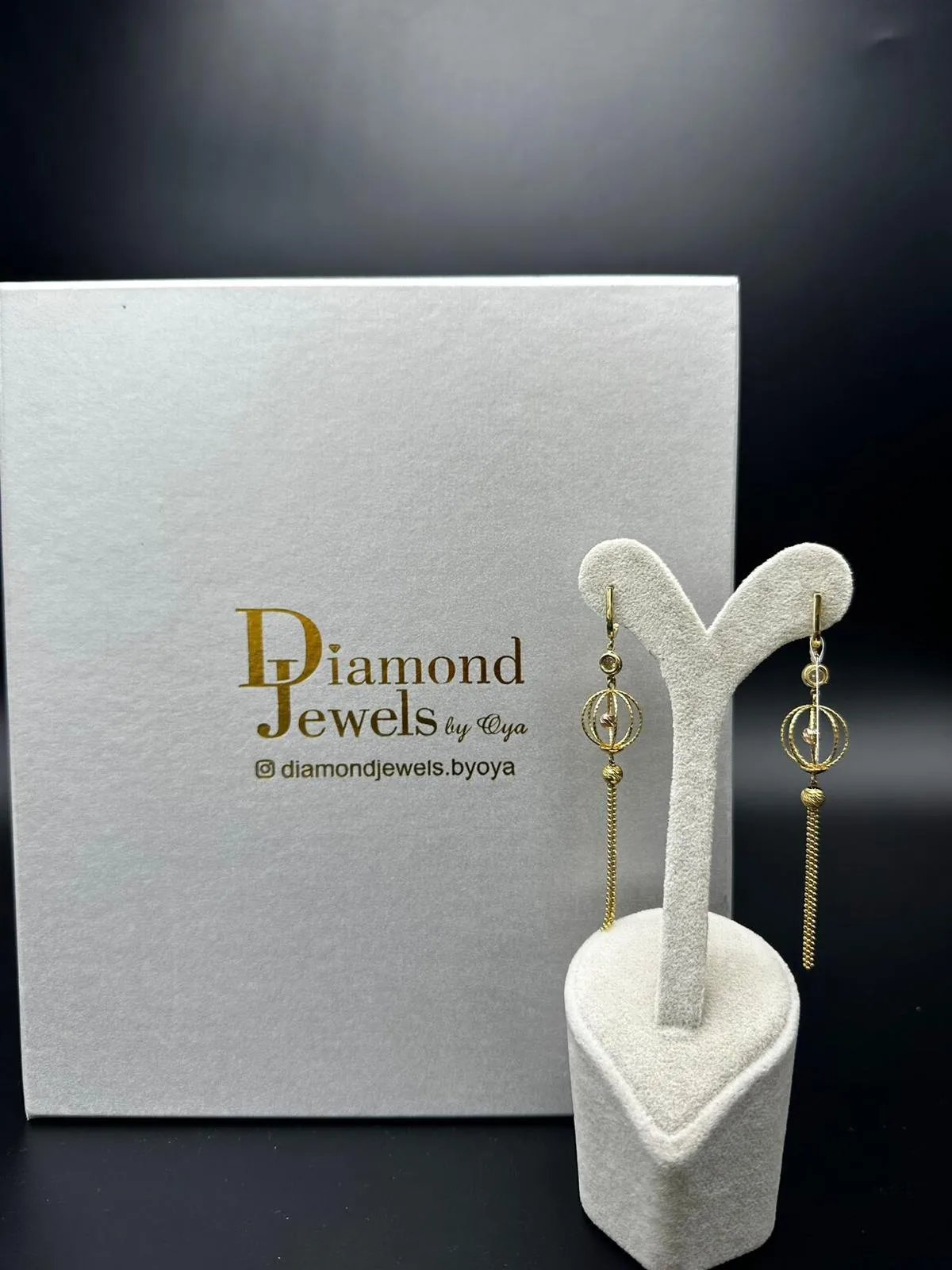 Goldene Ohrhänger mit Kugeln vor einer Diamond-Jewels-Schachtel