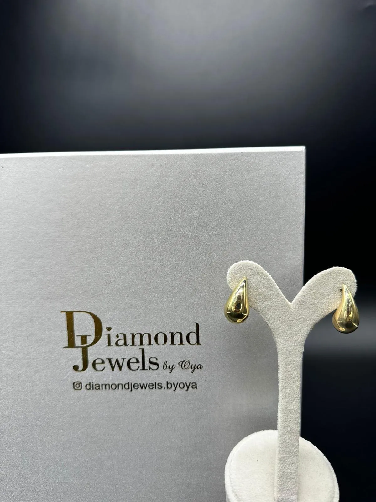 Goldene Tropfen-Ohrringe vor einer Diamond-Jewels-Schachtel