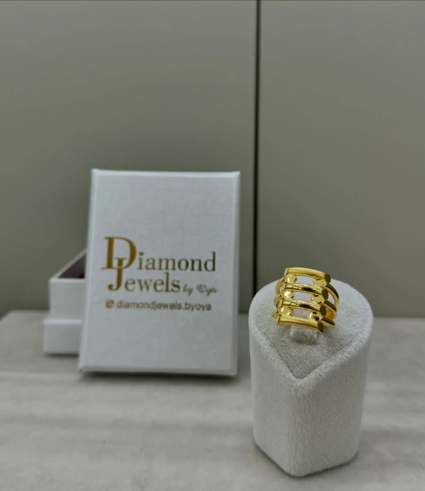 Breiter mehrreihiger Goldring auf einem Ringständer vor einer Diamond-Jewels-Schachtel
