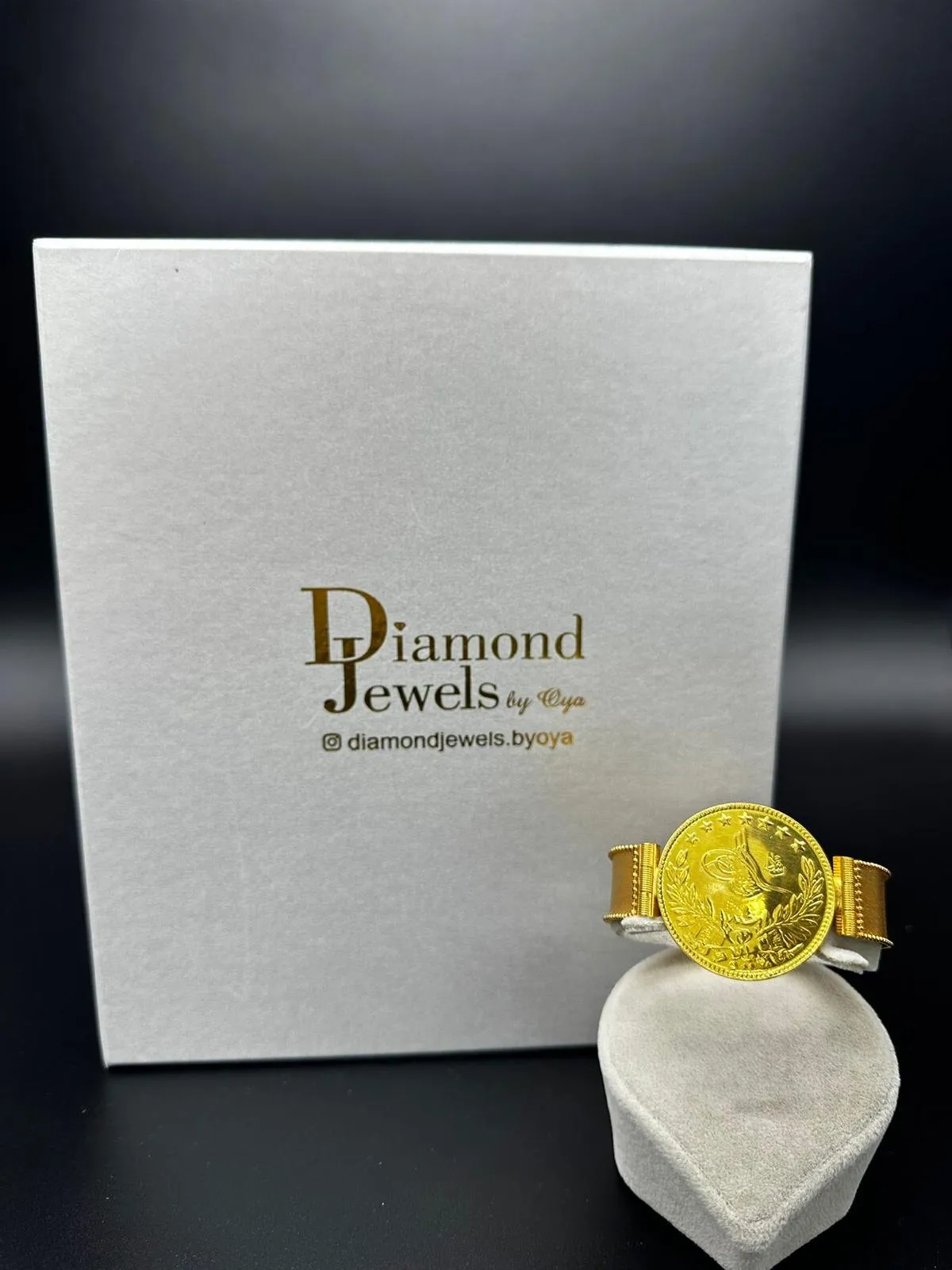 Breiter Goldring mit Münze vor einer Diamond-Jewels-Schachtel