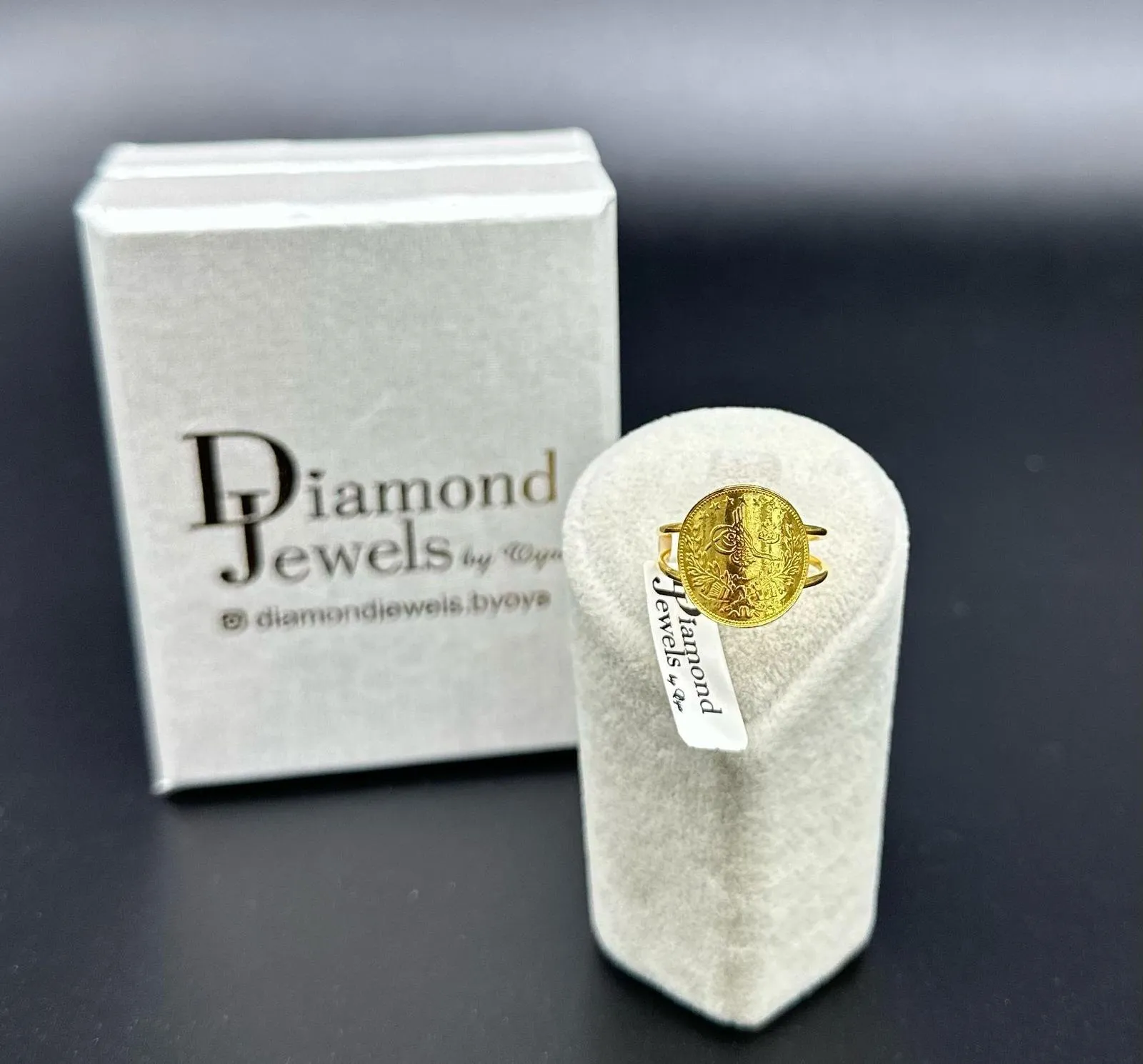 Goldring mit Münze auf einem Ringständer vor einer Diamond-Jewels-Schachtel