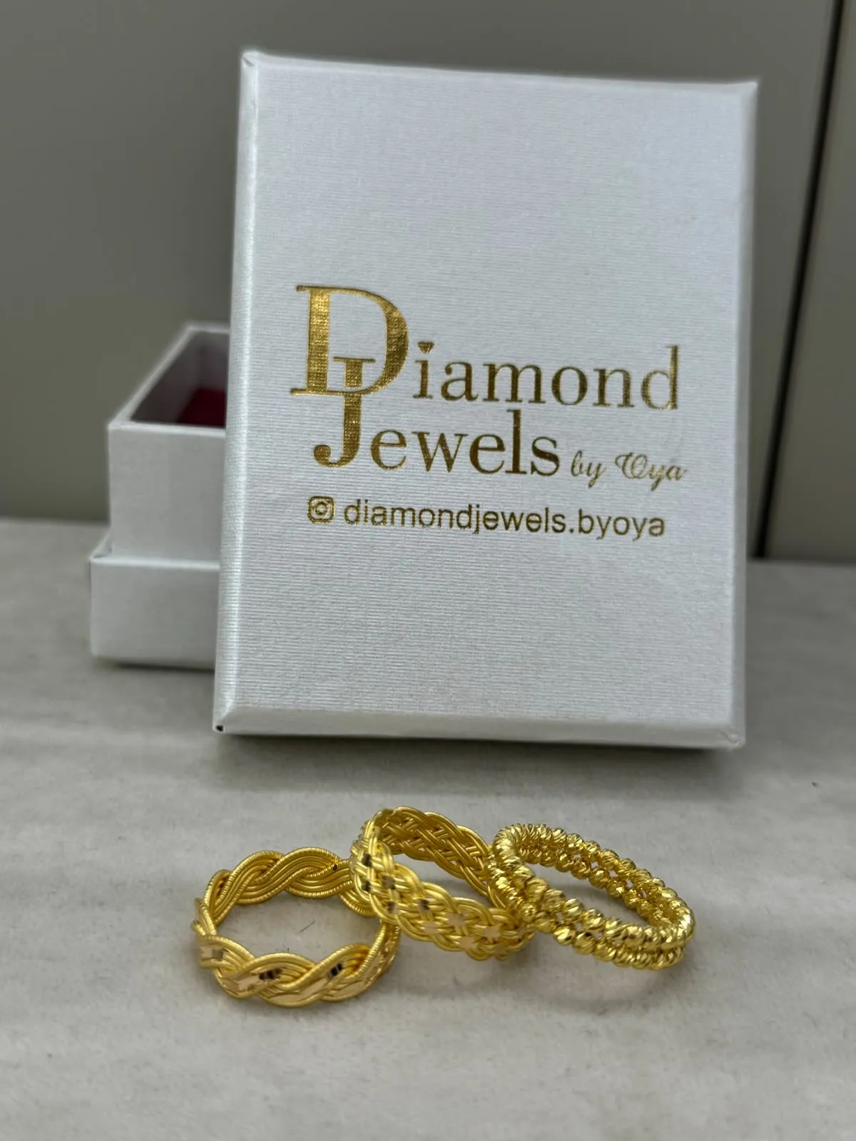 Drei geflochtene Goldringe vor einer Diamond-Jewels-Schmuckschachtel